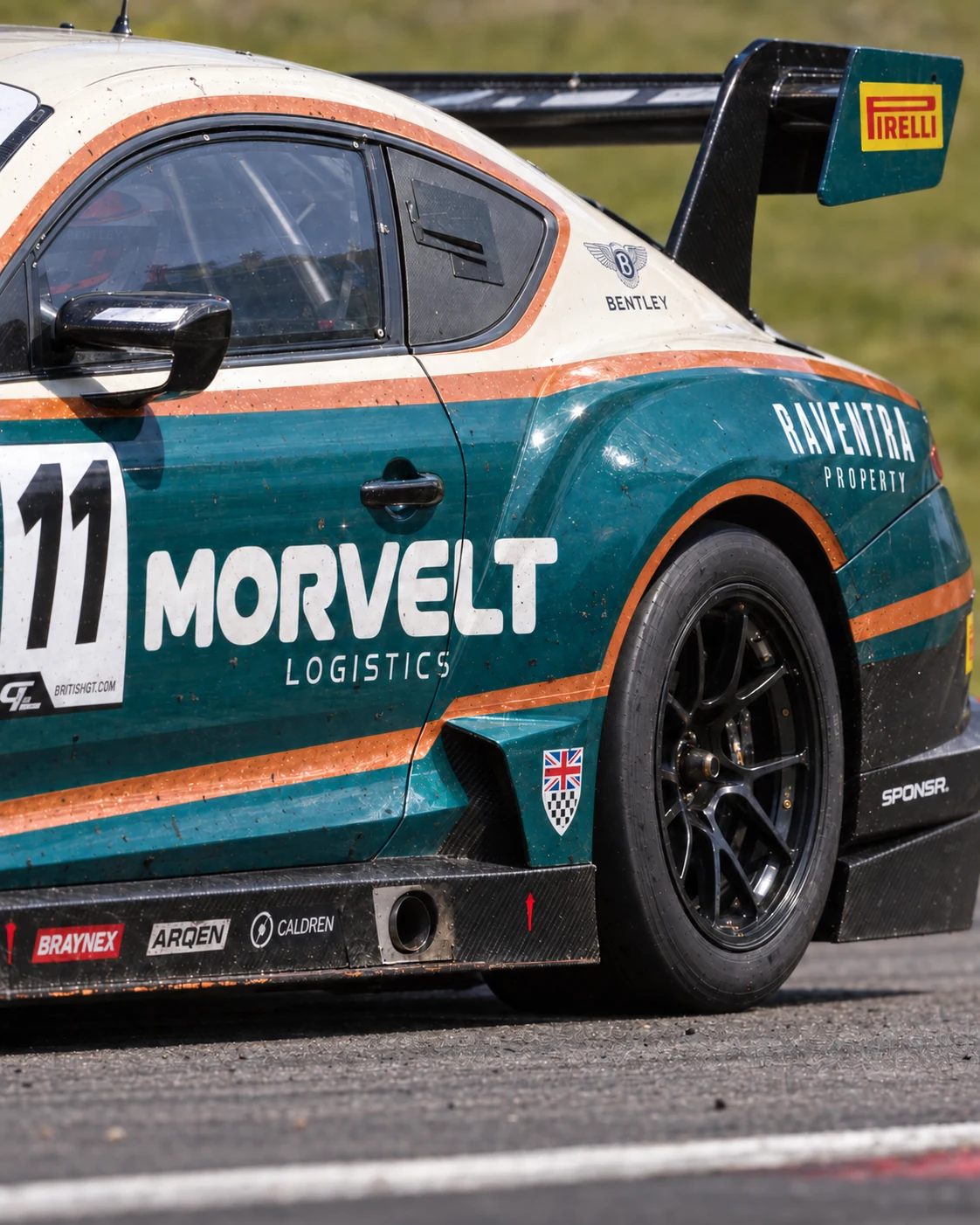 The haunch of a dark green GT car, bodywork reflecting the pit lane (SPONSR livery concept).