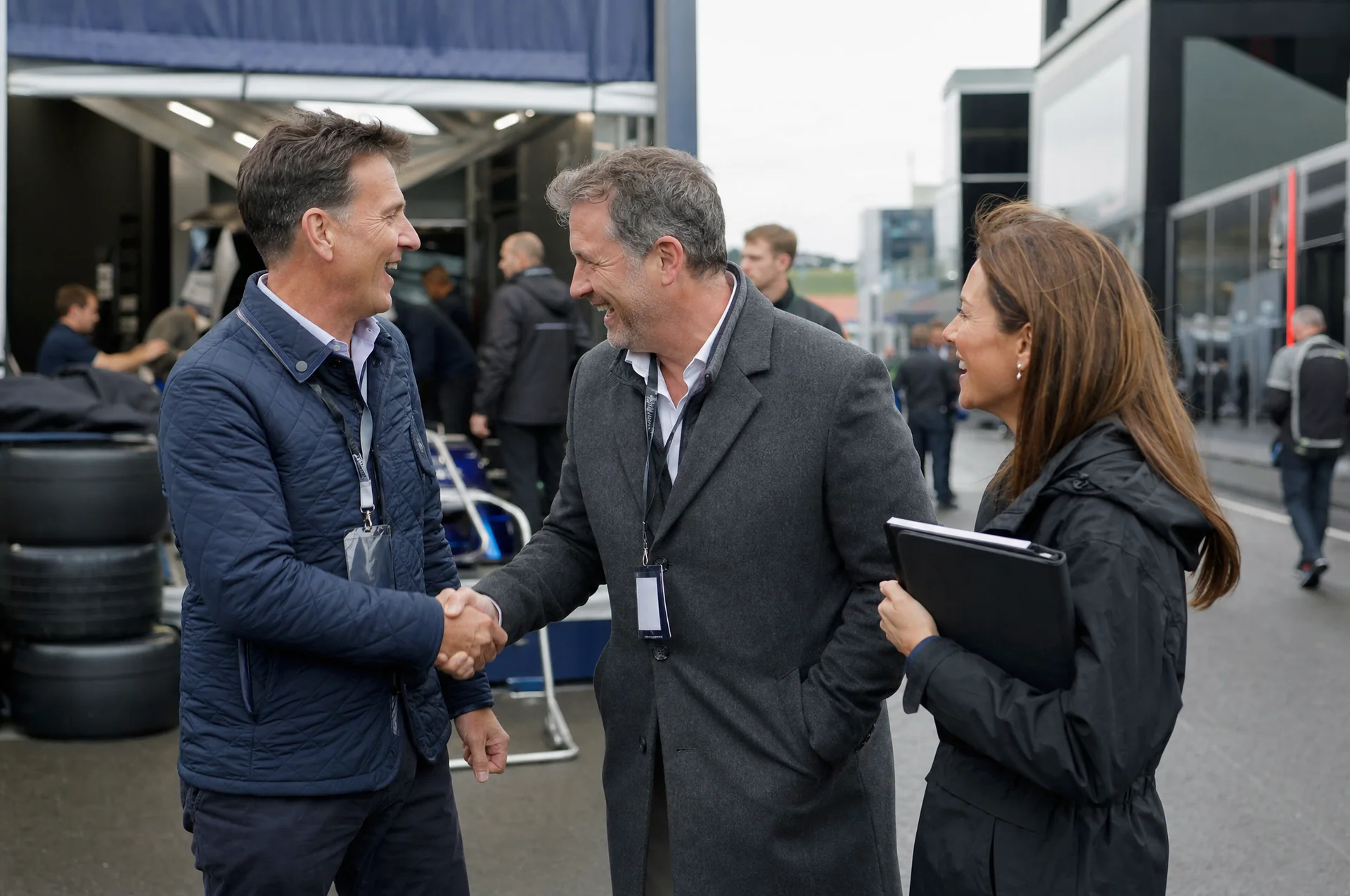 Two business owners shaking hands and laughing between race transporters in the paddock, a SPONSR host introducing them.